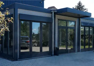 Moderne Containeranlage mit großer Fensterfront, Materialmix aus lakietem Stahl und gestaltetem Aluminium