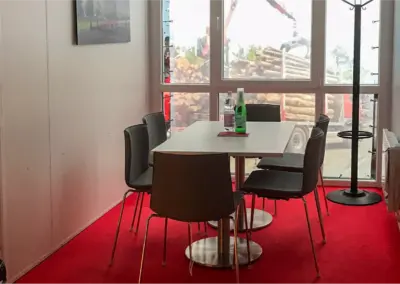 Besprechungsraum in einem MBN-Messecontainer ausgestattet mit roten Teppichbelag, Besprechungstisch und Stühlen vor einer Fensterfront