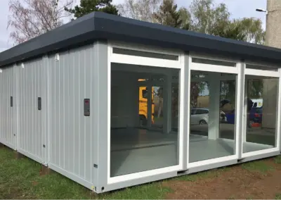Moderner MBN Modulwelt Bürocontainer mit großen Glasfronten und heller Innenfläche, aufgestellt im Außenbereich neben einem Gebäude.
