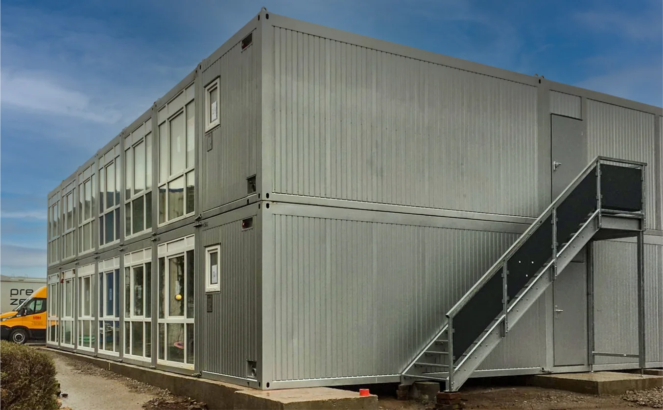 Zweigeschossige Containeranlage der Firma MBN Modulwelt mit Außentreppe und großen Fensterfronten, genutzt als modulare Büro- oder Arbeitsräume.