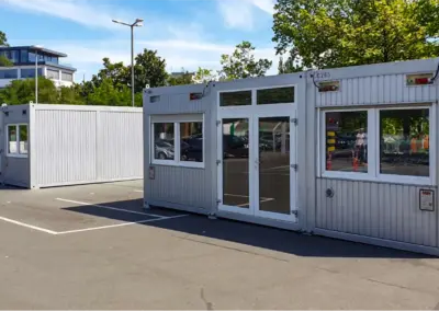 Mehrere modulare Container mit Fenstern und Türen, aufgestellt auf einem Parkplatz und geeignet für Gastronomie oder Verkauf.