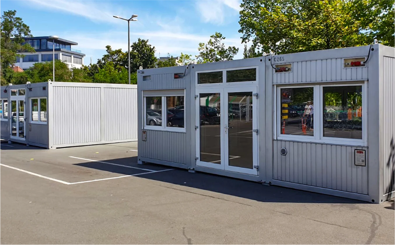 MBN Modulwelt Ausstellungscontainer Mehrere modulare Container mit Fenstern und Türen, aufgestellt auf einem Parkplatz und geeignet für Gastronomie oder Verkauf.