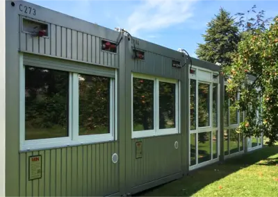Modulare Containeranlage mit großen Fenstern im Grünen, genutzt als Kindergarten- oder Aufenthaltsräume.