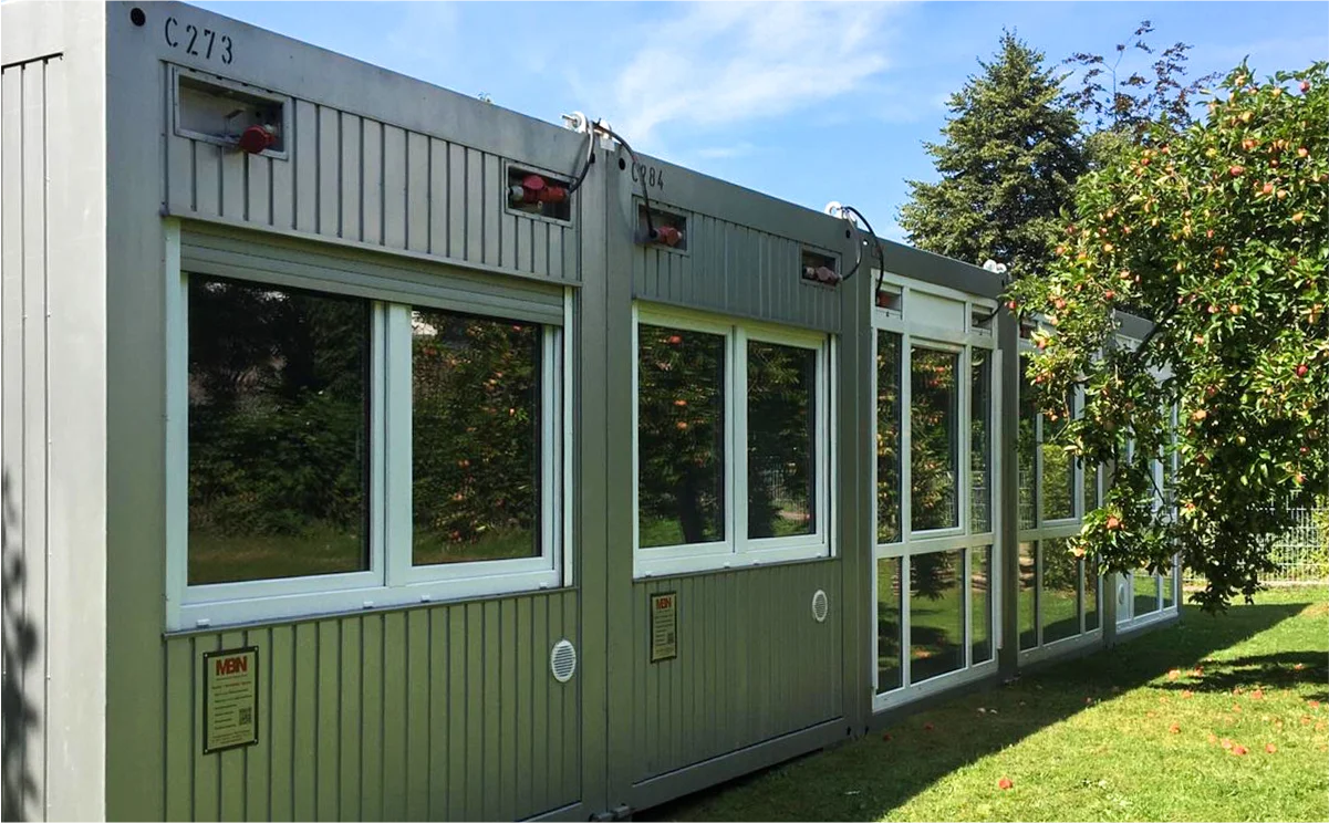 MBN Modulwelt Kindergartencontainer Modulare Containeranlage mit großen Fenstern im Grünen, genutzt als Kindergarten- oder Aufenthaltsräume.