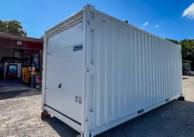 Weißer Lagercontainer mit Rolltor, aufgestellt auf einem Betriebsgelände.