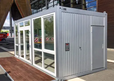 Verkaufscontainer mit großer Fensterfront und seitlicher Tür, aufgestellt im urbanen Umfeld.