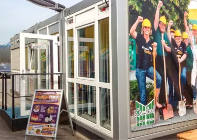 Verkaufscontainer mit Eingang und Werbebanner, genutzt als mobiler Shop auf einem Parkplatz.