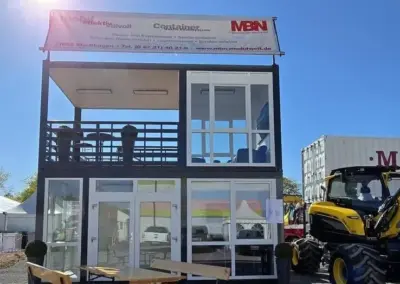 Moderner zweigeschossiger Messecontainer mit Glasfront, Dachterrasse und Sitzbereich auf einem Messegelände