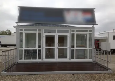 Moderner Bürocontainer mit großer Glasfront, Eingangstür und Holzterrasse