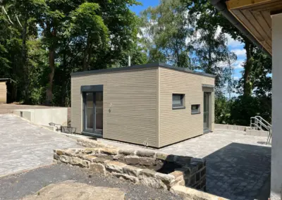 Modernes Tiny House aus zwei Containermodulen mit edler Holzoptik-Fassade, anthrazitfarbenen Fenstern und Terrasse im Grünen.