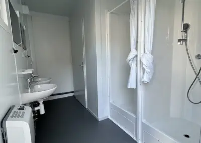 Moderne Innenausstattung eines Sanitärcontainers mit zwei Duschkabinen, weiße Waschbecken, Spiegel und Elektroheizung.
