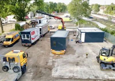 Luftaufnahme der Montage von MBN Modulwelt-Containern mit LKW-Ladekran und Mobilbagger auf einem Baustellengelände.