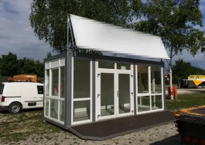 Moderner Bürocontainer mit großer Glasfront, Eingangstür und Holzplattform auf einem Außengelände