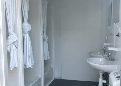 nnenansicht eines MBN Modulwelt Duschcontainers mit drei Duschkabinen samt Duschvorhängen, zwei Waschbecken, Spiegeln und dunkelgrauem Boden.