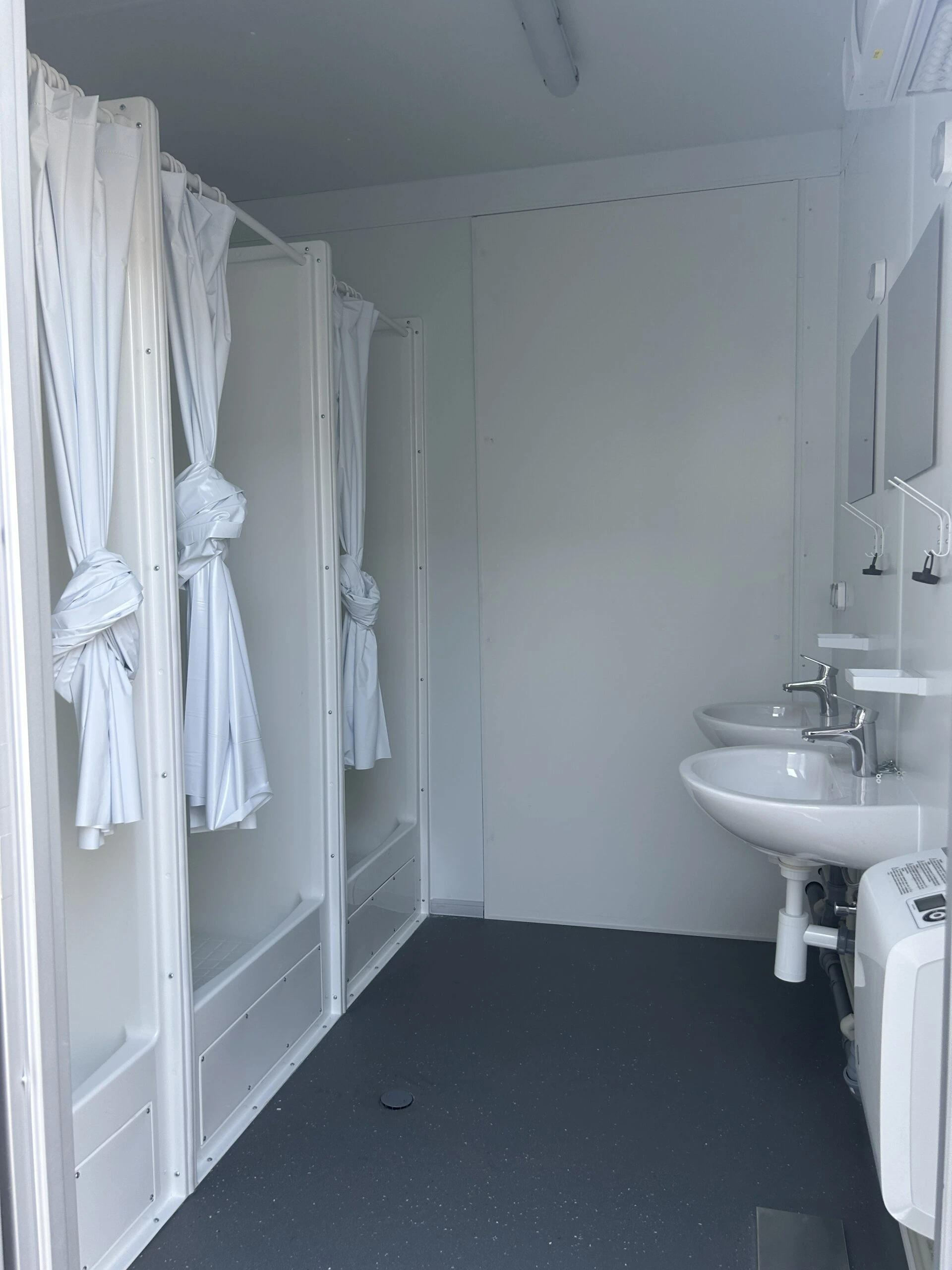 MBN Modulwelt Duschcontainer – Innenansicht mit Duschkabinen & Waschbecken nnenansicht eines MBN Modulwelt Duschcontainers mit drei Duschkabinen samt Duschvorhängen, zwei Waschbecken, Spiegeln und dunkelgrauem Boden.