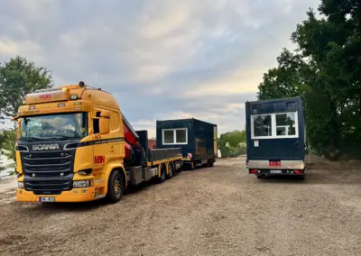 Gelber Scania Kran-LKW von MBN mit Anhänger transportiert anthrazitfarbene Containermodule für den Aufbau einer modernen Containeranlage.